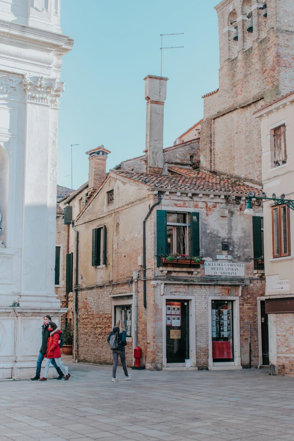 Persone passeggiano in una piazza storica fiancheggiata da edifici in pietra.